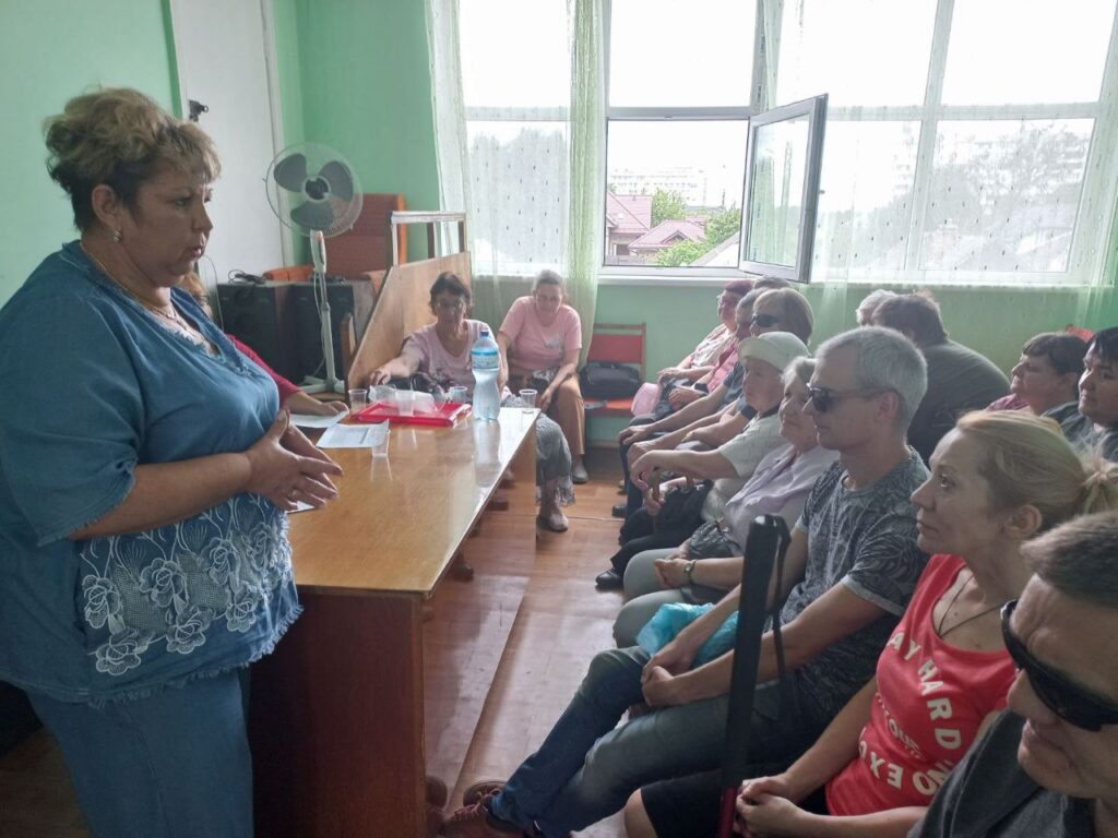 На фото жінка голова УТОС Алла Козлова і члени організації, яки приймають участь в громадських консультаціях, сидять в приміщенні.